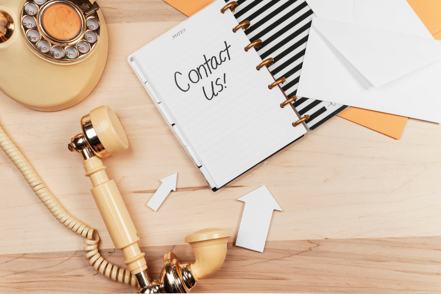 Vintage telephone and notebook with 'Contact Us!' on a wooden surface